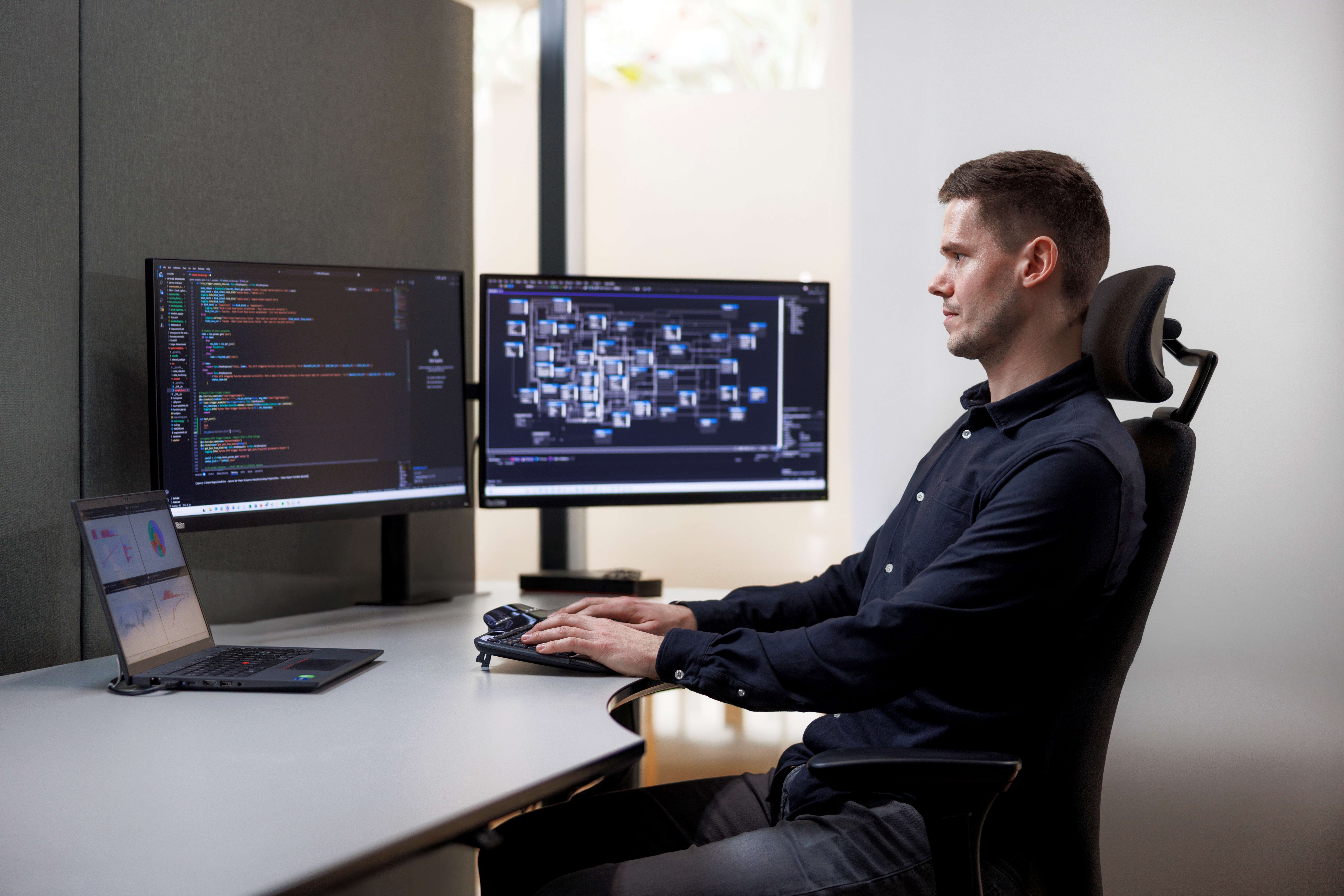 Magnus Gribbestad ved skrivebordet med kode og datamodeller på skjermene